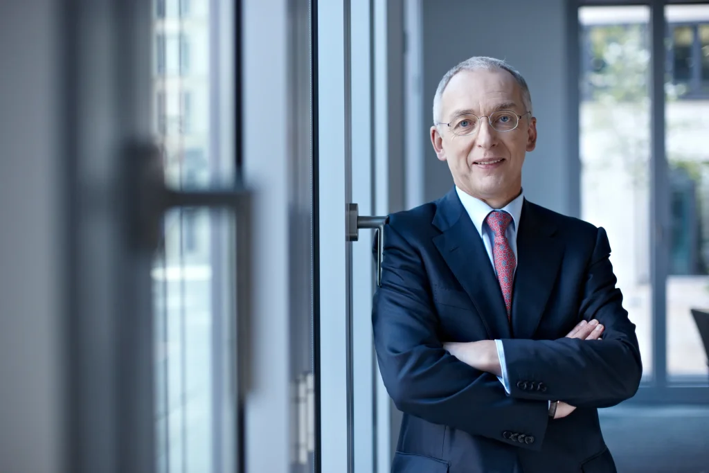 Verhandlungstrainer Hermann Schlindwein steht an einem Fenster und schaut lächelnd in die Kamera