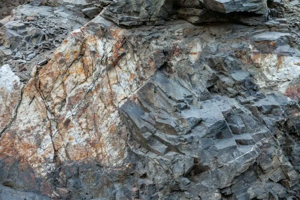 Nahaufnahme einer rauen Felsstruktur mit grauen, braunen und rostfarbenen Schichten und Rissen